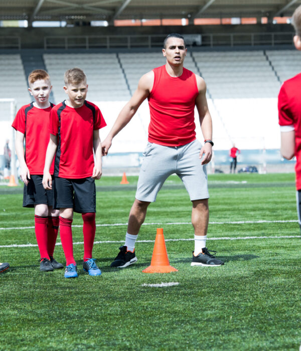 Full length portrait of handsome Latin-American football coach giving instructions to group of teenage boys during practice on field in stadium, copy space
